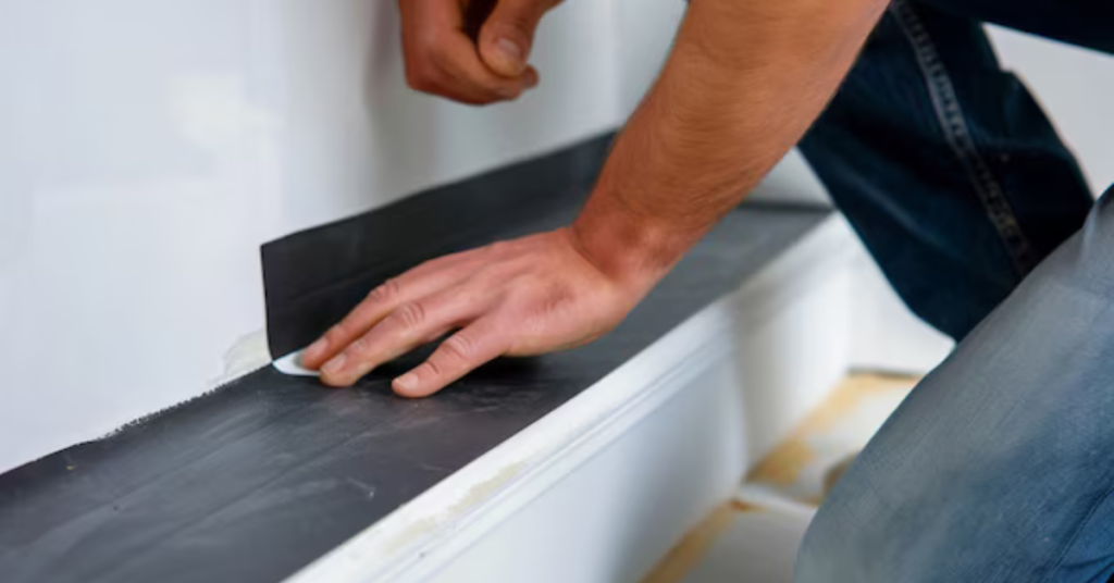 A-man-is-seen-placing-black-tape-on-a-wall-ensuring-effective-waterproofing-in-the-bathroom.