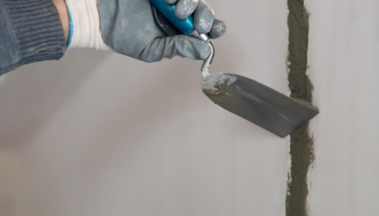 Close-up-of-a-gloved-hand-using-a-trowel-to-apply-sealant-or-filler-to-a-vertical-wall-crack-during-a-wall-repair-process